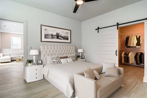 Huntsville, AL Luxury Apartments for Rent - The Collins - Bedroom with Wood-Style Flooring, White Walls, Large Bed, Nightstands with Lamps, Settee Bench, Ceiling Fan, and Spacious Closet.